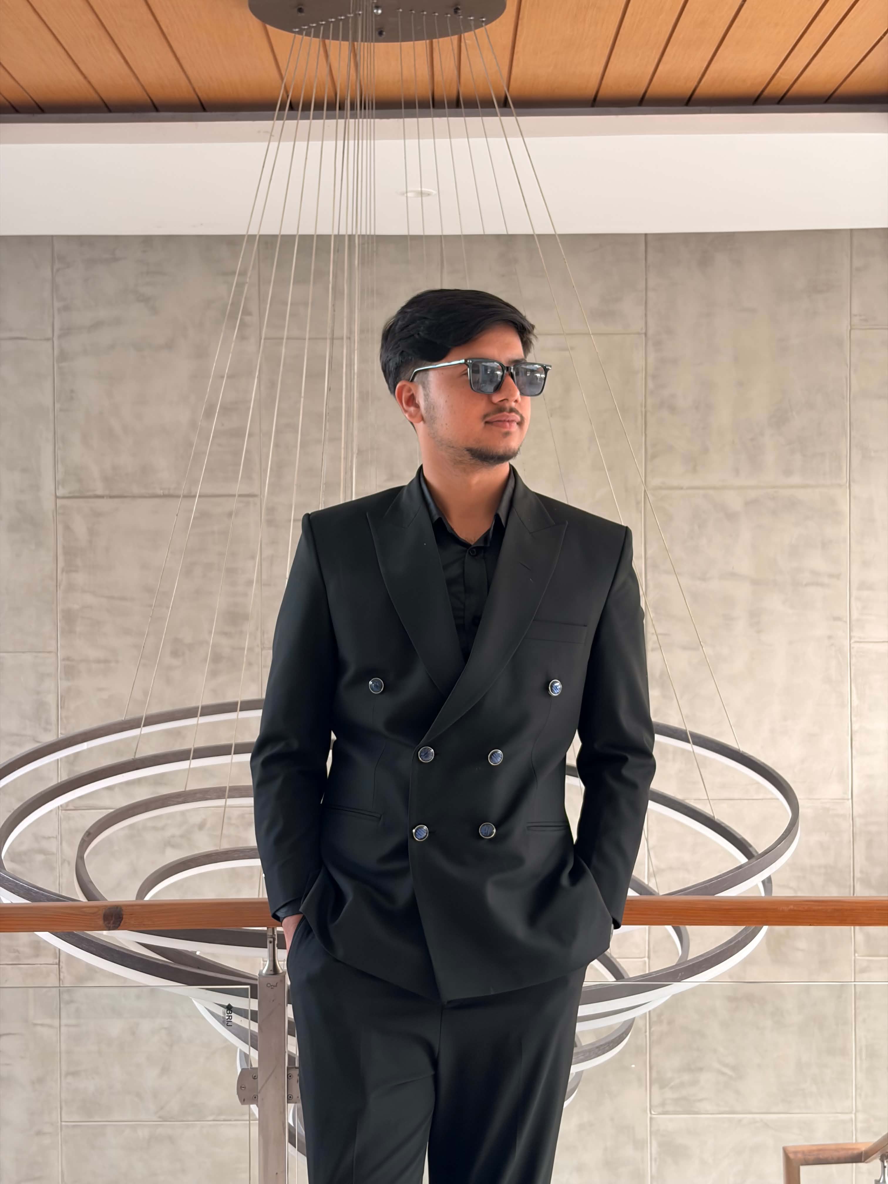 Bipson Paudel in a black double-breasted suit and sunglasses, standing in a modern interior